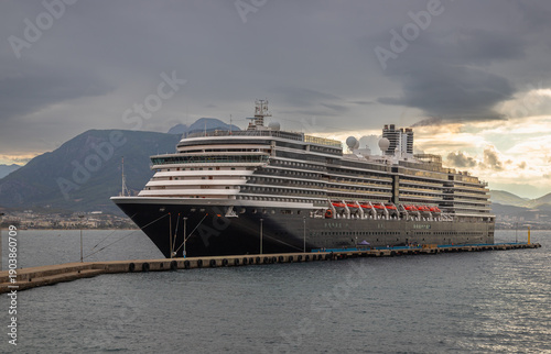 Canvastavla Large modern cruise ship docked at a concrete pier under dramatic cloudy skies with mountains in the background