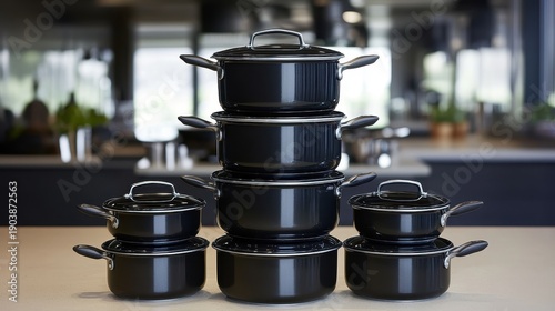 A neat stack of black cooking pots and pans with lids arranged in a kitchen setting
