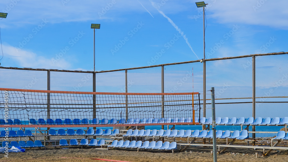 Fototapeta premium Beach volleyball court with blue seating and net under clear sky