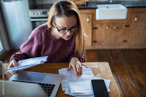 Woman reviewing household bills at home kitchen table