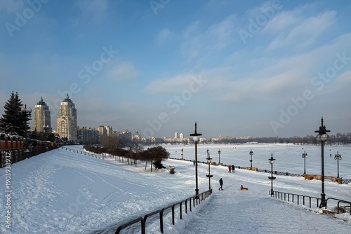 Panoramic winter riverfront promenade with snowy steps and frozen bay under cloudy sky