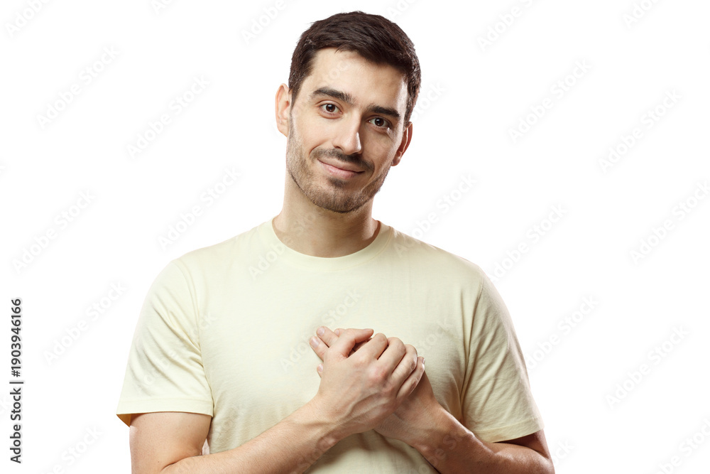 Obraz premium Kind hearted friendly nice guy shows kindness, wearing blank biege t-shirt. Portrait of smiling positive young man keeps hands on chest, expresses sympathy