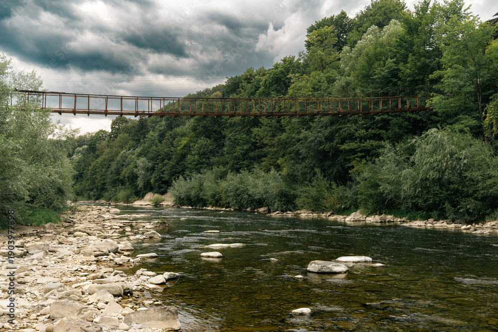 Fototapeta premium Suspension Bridge Over Mountain River in Forest Landscape