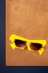 Sunglasses on geometric yellow paper cutout on textured terracotta