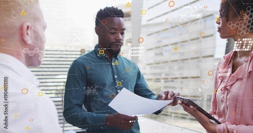Holding paper, mid-age man in teal shirt reading document in office, with tablet and data overlay