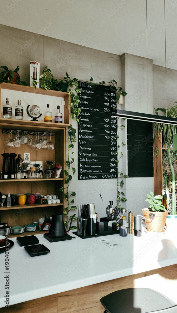 Fototapeta premium Modern cozy coffee shop interior with bar counter, shelves, menu board and indoor plants. Calm urban atmosphere with vintage tones and film grain, soft natural light