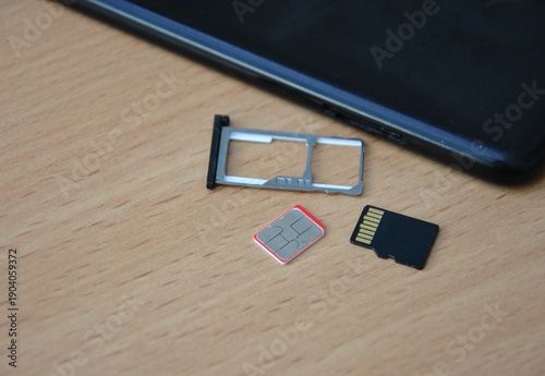 Mobile phone SIM card and flash memory card with tray on a table. Digital technology and telecommunication hardware.