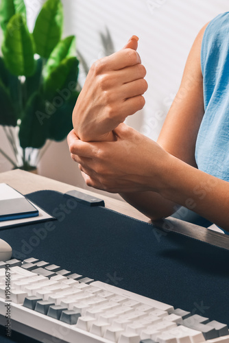 Severe pain in the hand or wrist after using a computer mouse and keyboard. A woman massages her wrist at an office desk. Vertical photo.