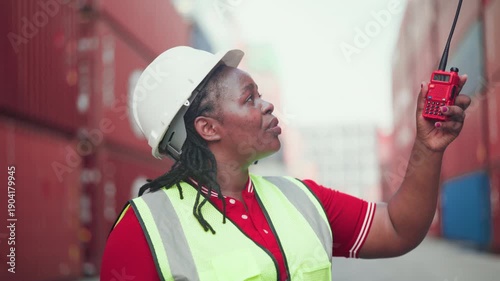 Close-up portrait of a happy Black woman working in logistics, wearing a hard hat and safety vest at a shipping port. Concept of job satisfaction and industrial career.