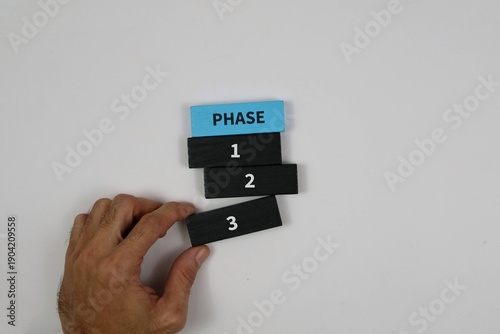 Fotografie hand arranging numbered phase blocks (1, 2, 3) beneath a blue PHASE tile against an white background, symbolizing project planning and step-by-step progress