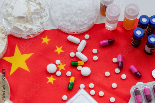 Photography A Chinese medicine production, pharmaceuticals concept with a close up of medicine base substances in trays and various loose and packaged tablets and capsules on the Chinese flag