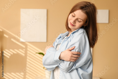 Beautiful young happy woman hugging herself at home