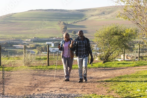 Senior african american couple with backpacks walking in sunny nature