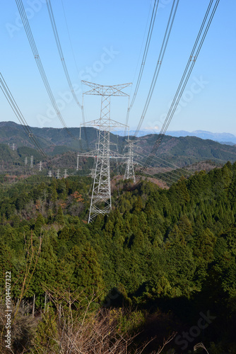 山並みを越えて連なる送電鉄塔と高圧電線の風景