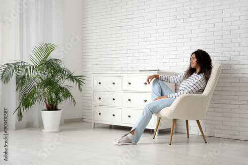 Young African-American woman sitting in white armchair at home