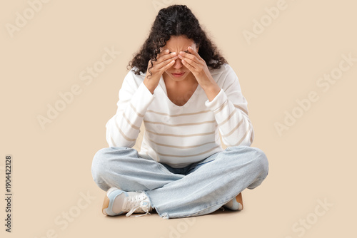 Young African-American woman having panic attack on beige background