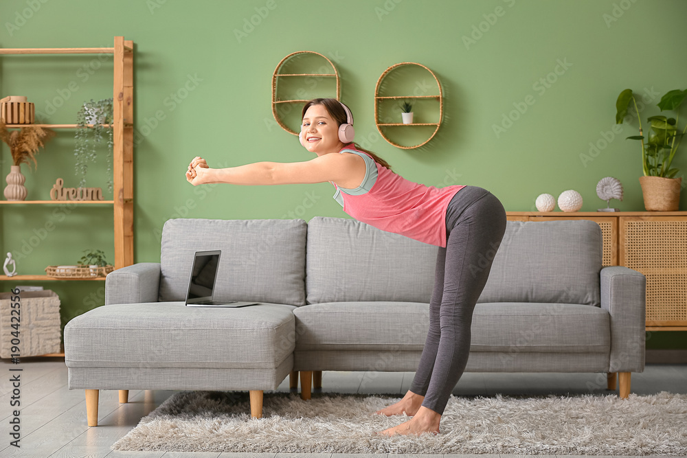 Naklejka premium Beautiful young woman in headphones practicing yoga in living room