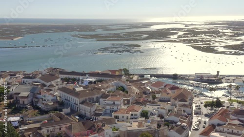 Aerial forward flight over Faro city at sunset towards the lagoon, sun
