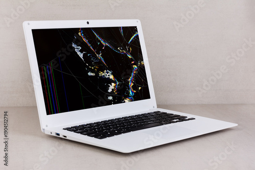 white laptop with a broken screen in color spots and cracks on a gray background close up