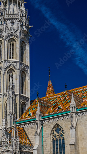 Konstfotografi Photography of a tall, ornate Gothic church tower with a colorful mosaic roof, captured on a sunny day against a bright blue sky