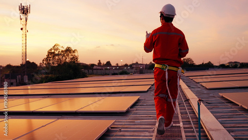A solar technician in an orange jumpsuit walks across a rooftop solar array at sunset. Renewable energy maintenance, green infrastructure, and sustainable power solutions