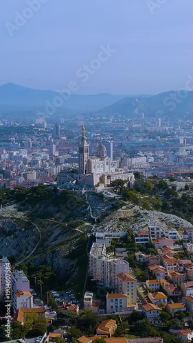 4K aerial vertical video of Notre-Dame de la Garde basilica. Aerial view of Marseille city skyline, mountains, and iconic hilltop church. Vertical video for France travel reels.