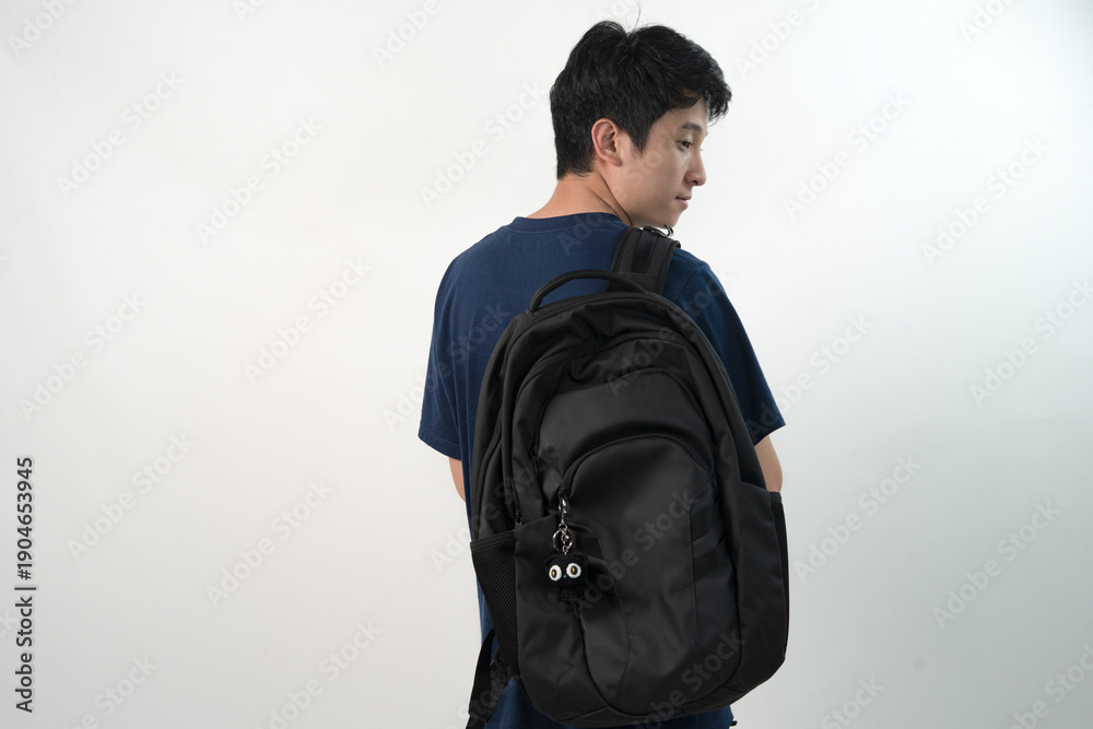 Fototapeta premium Side view of a young Asian man wearing a black backpack decorated with a small black handmade crochet cat for mockup or branding