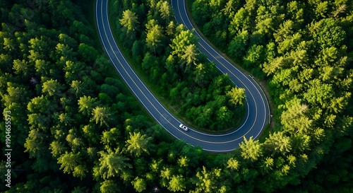 Sharp hairpin curve on mountain road winding through lush green forest with white car navigating asphalt track
