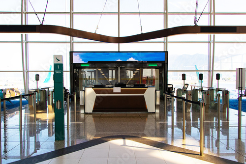 Airplane boarding gate. Bright interior of airport terminal gate exit zone follows to aircraft boarding area with ticket check desks in foreground, computer monitors, information screens on top.