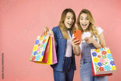 Happy women looking at smartphone checking big sale together isolated on pink with empty space for text