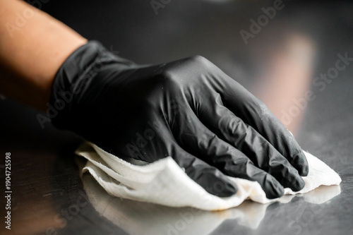 Canvastavla A close-up shot of a person wearing a black nitrile glove using a white cloth to