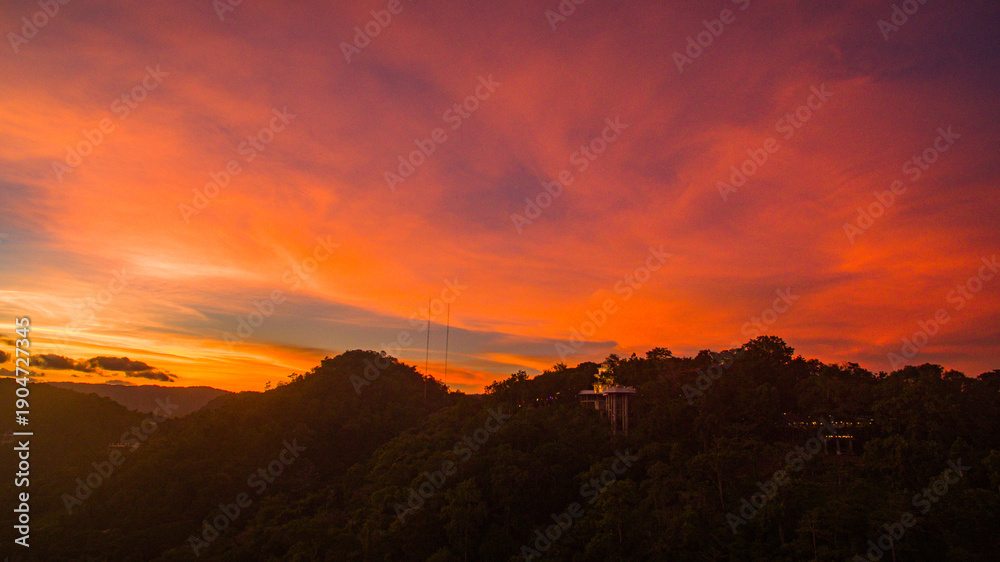 Fototapeta premium Aerial view of scenery Khao Rang viewpoint at twilight. view of a town nestled among lush green mountains at sunset, with a Pavilion structure perched on the hillside at Phuket town at Dusk