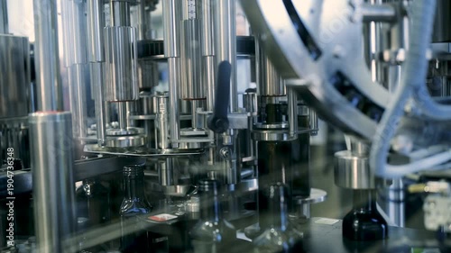 Close up of dark glass bottles moving on a conveyor belt during the automated filling and capping process in an industrial olive oil manufacturing plant.