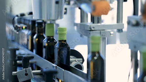 Close up of dark glass bottles moving on a conveyor belt during the automated filling and capping process in an industrial olive oil manufacturing plant.