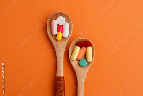 Various colorful prescription antibiotic capsules, vitamin pills and tablets in wooden spoons on orange background. Ideal for healthcare, pharmaceutical treatments, 