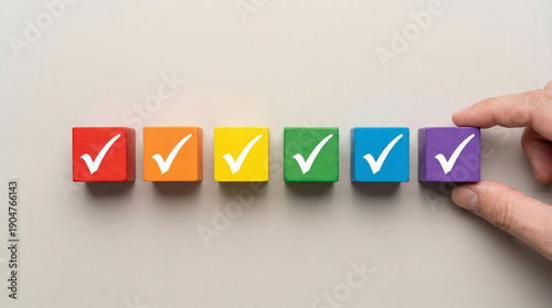 hand places colorful wooden block with checkmark, completing row of similar blocks. It symbolizes task completion, goal achievement, or project success. sense of accomplishment and progress.
