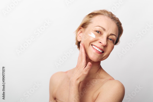 Cuadro en lienzo Smiling middle aged woman applying face cream on cheek with hand touching skin