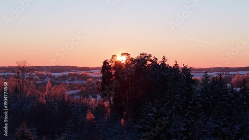 4K aerial drone right move through Lithuania winter forest at golden hour, sun rays shining through frosted trees, cinematic landscape with warm sunset colors