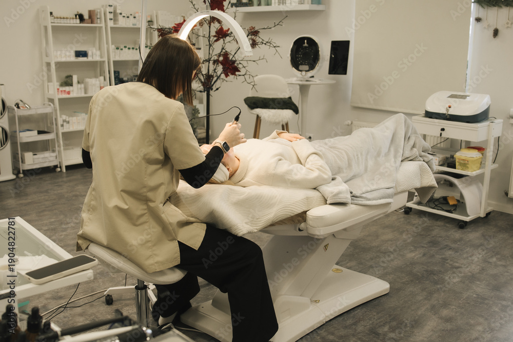 Fototapeta premium Johvi, Estonia – December 24, 2026: A woman undergoes an IPL facial cosmetic procedure using light-based aesthetic equipment in a beauty clinic. Real clinical environment during a professional cosmeto