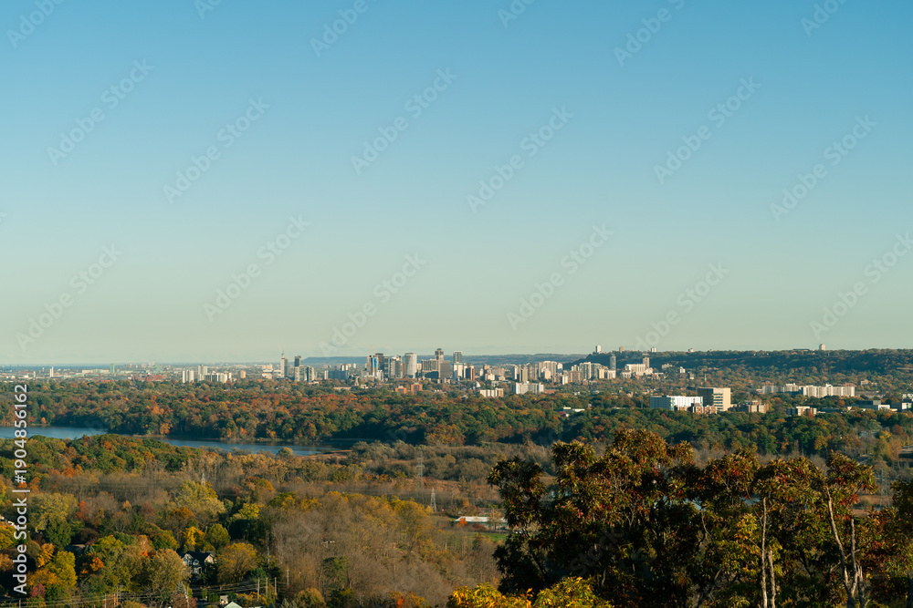 Fototapeta premium Panoramic of Hamilton, Ontario in Canada, skyline rising above colorful autumn forest, capturing urban landscape surrounded by fall foliage.