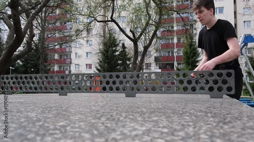 Dynamic outdoor table tennis match in a sunny park. Players actively hitting the ball with rackets on a concrete table, green grass and playground visible in the background. Captures fun, competitive 