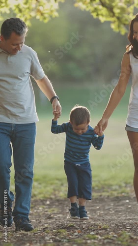Cute young family walking in the park - parents holding their little son by his hands