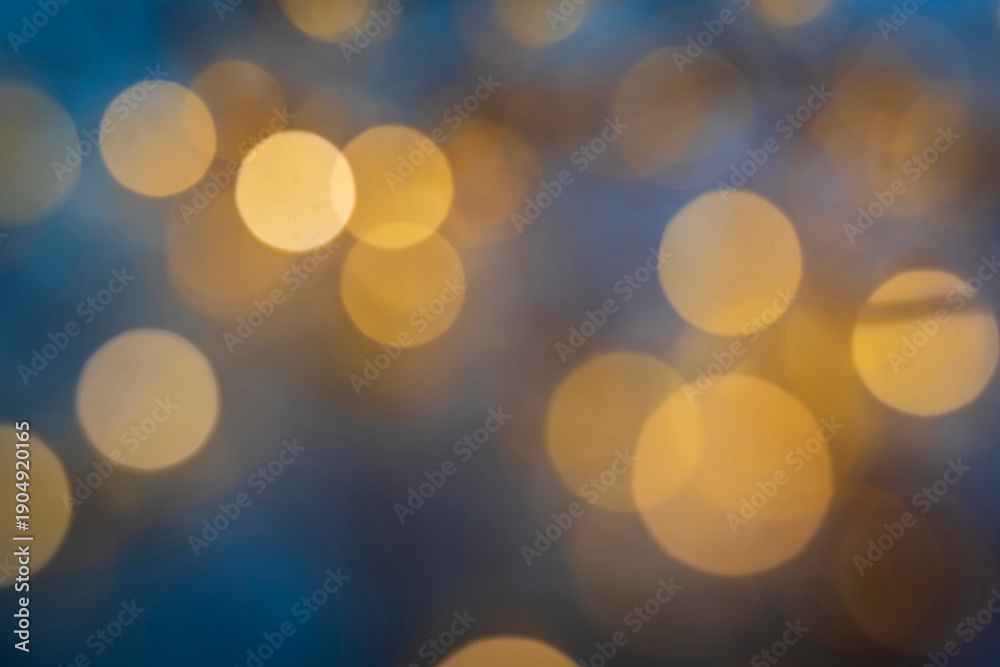 Obraz premium Abstract golden bokeh circles on blue background, soft blur. Warm yellow bokeh light circles glowing against a dark blue background in a soft focus.