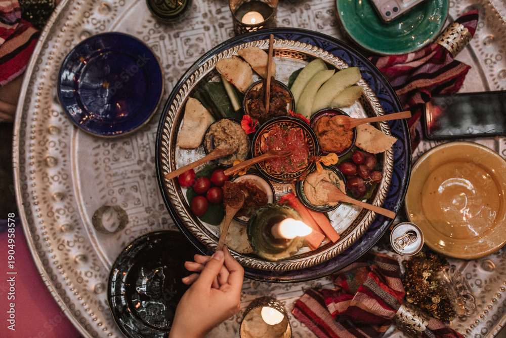 Obraz premium Top view of shared iftar platter with dips, bread, fruit and candlelight, capturing the warmth of Ramadan family meals, hospitality and gratitude