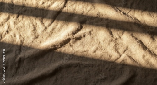 Close-up of beige textured fabric with deep shadows and warm sunlight streaks