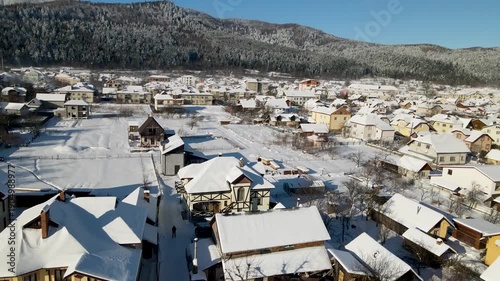 Houses in a village near snow-covered mountains with pine trees in winter. Aerial panoramic drone view from above, top view from drone.  Ukraine, Carpathians, Skole city
