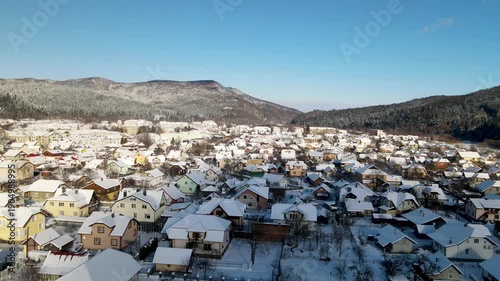 Houses in a village near snow-covered mountains with pine trees in winter. Aerial panoramic drone view from above, top view from drone.  Ukraine, Carpathians, Skole city
