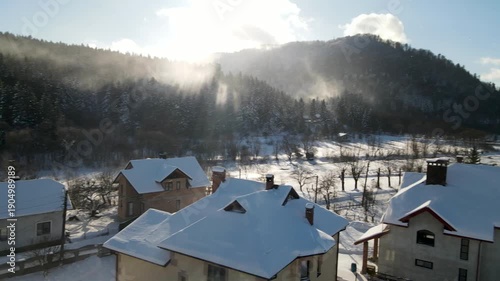 Aerial drone view of houses in a village near snow-covered mountains with pine trees in winter. Aerial panoramic drone view from above, top view from drone.  Ukraine, Carpathians, Skole city
