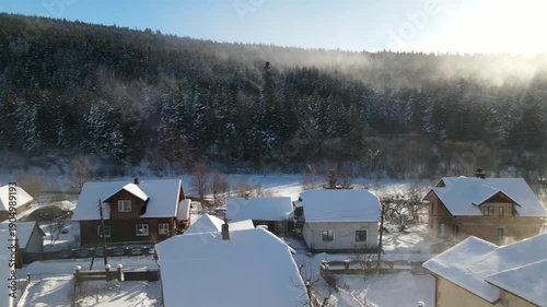 Aerial drone view of houses in a village near snow-covered mountains with pine trees in winter. Aerial panoramic drone view from above, top view from drone.  Ukraine, Carpathians, Skole city
