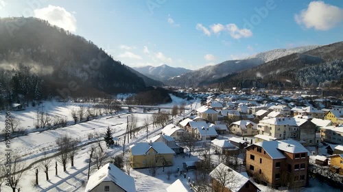 Aerial drone view of houses in a village near snow-covered mountains with pine trees in winter. Aerial panoramic drone view from above, top view from drone.  Ukraine, Carpathians, Skole city

